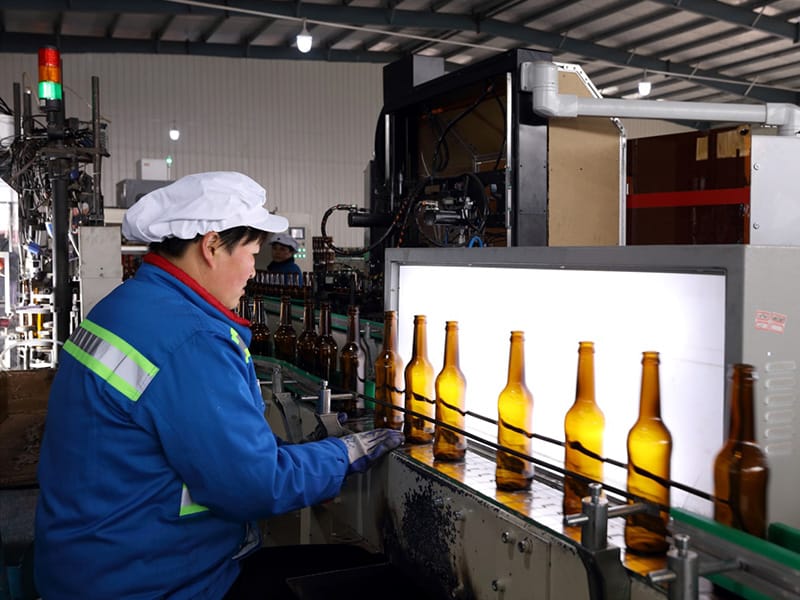 Amber glass beer bottles backlit at the inspection station of our Tai'an base