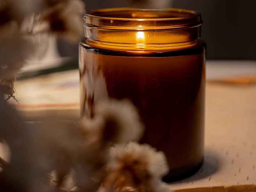 Amber glass candle jar burning on a warm neutral surface