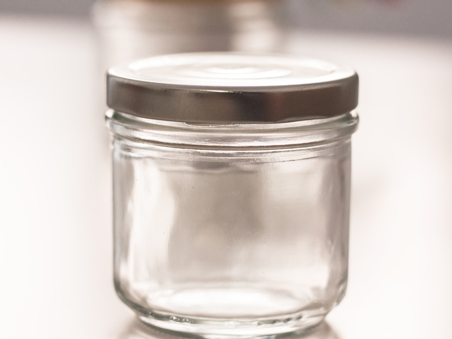 Empty clear glass jar with a metal lid on a soft grey backdrop
