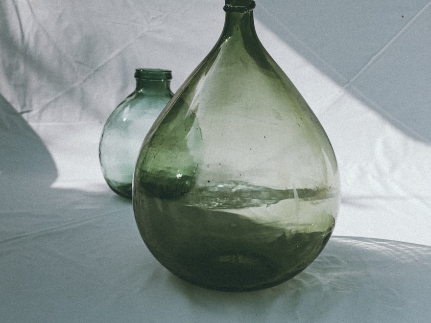 Large green glass demijohn vase on a pale surface