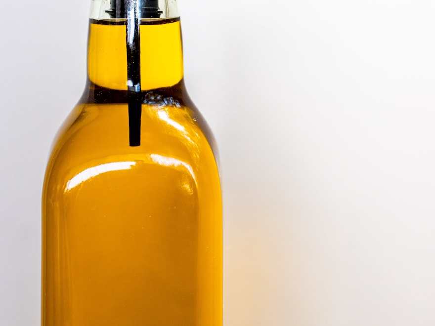 Amber glass olive oil bottle with a pour spout on a pale backdrop