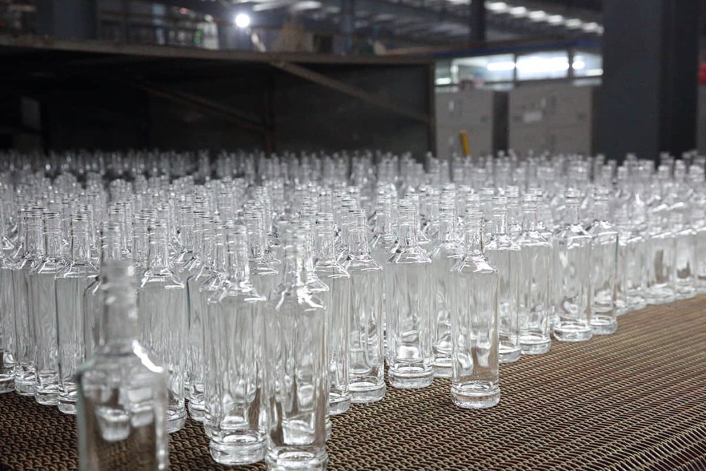 Rows of empty glass bottles on the cold-end conveyor inside SGSBOTTLE's glass bottle factory