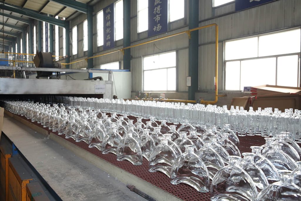 Rows of custom-shaped clear glass bottles leaving the annealing lehr at the SGSBOTTLE factory