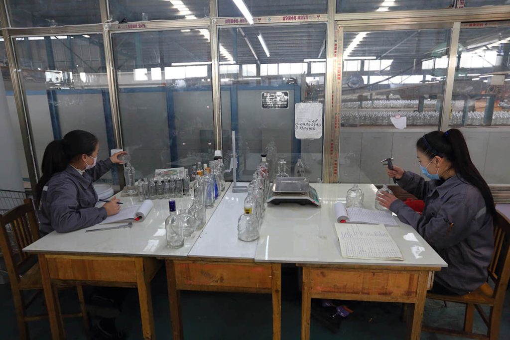 Quality inspectors checking glass bottles at the SGSBOTTLE factory QC station
