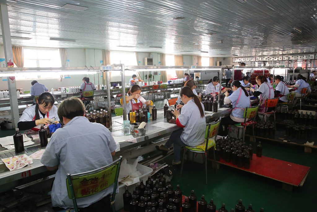 Decoration workshop at the SGSBOTTLE factory — operators applying decals to amber glass bottles