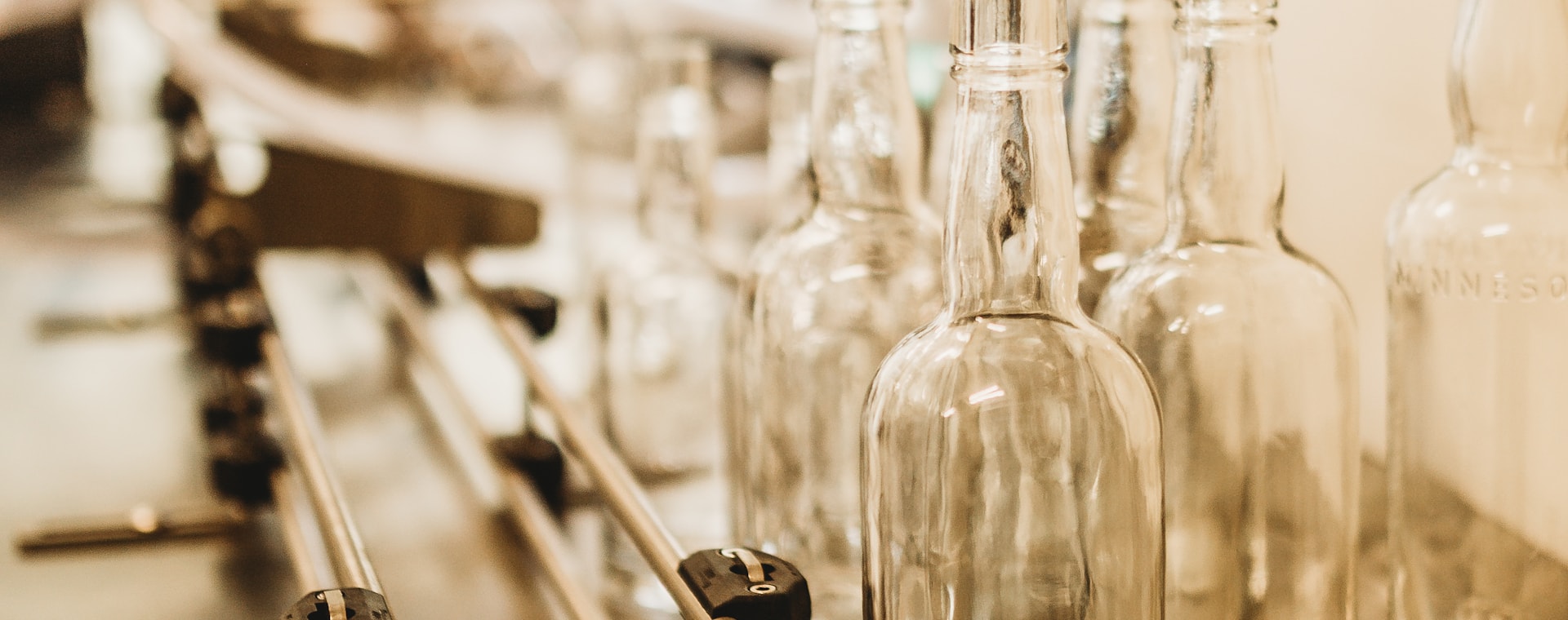 Rows of empty clear glass bottles moving along the cold-end line at a glass bottle factory